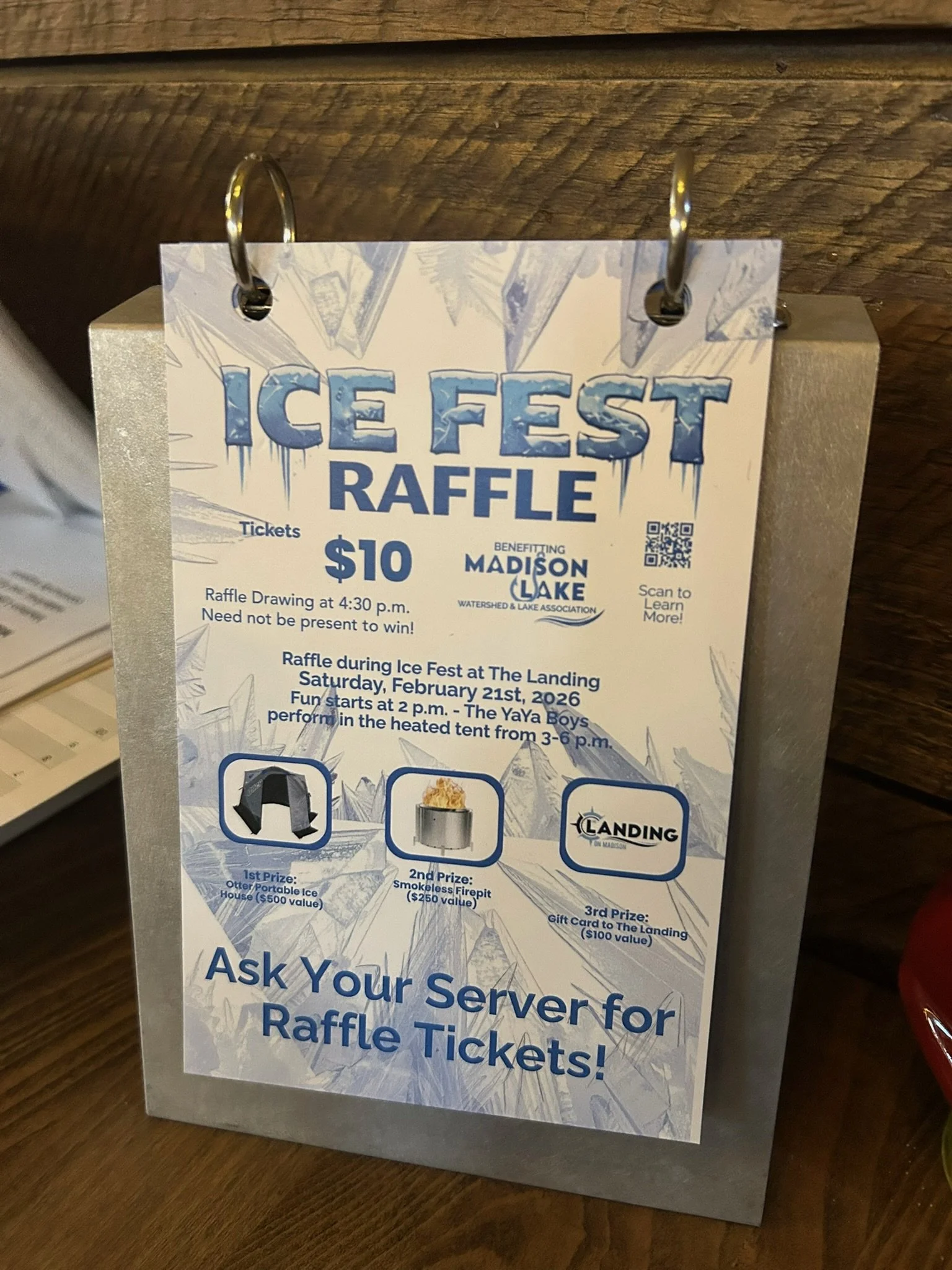 A raffle ticket for Ice Fest Raffle, benefiting Madison Lake Watershed & Lake Association. Ticket price $10, with a drawing at 4:30 p.m. on Saturday, February 21, 2026. Prizes include otter portable ice house, smokeless firepit, and a gift card to Th