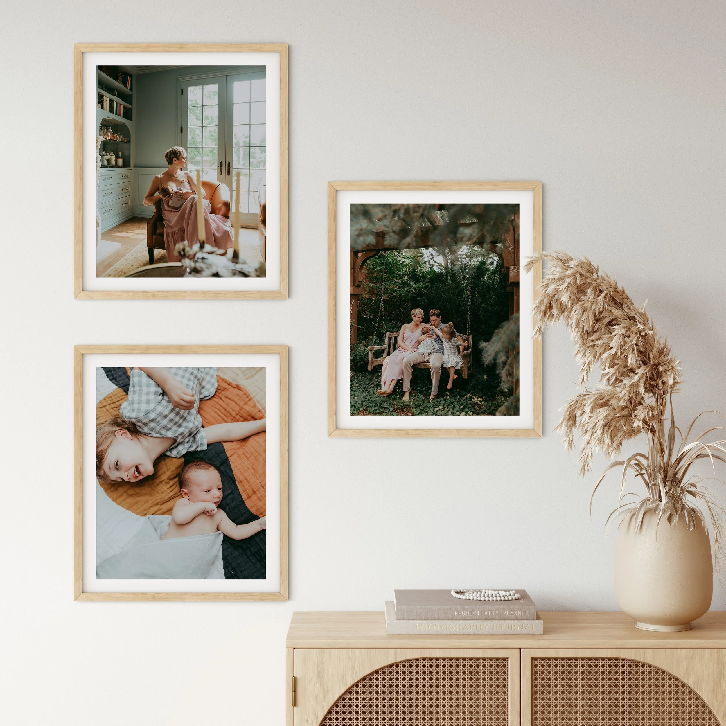 Living room wall with three framed photographs, a stack of books, and decorative dried pampas grass in a beige vase.