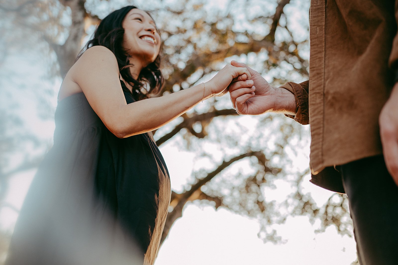 Pregnant woman in black dress holding husband's hand during photo session with Sunshine Lady Photography