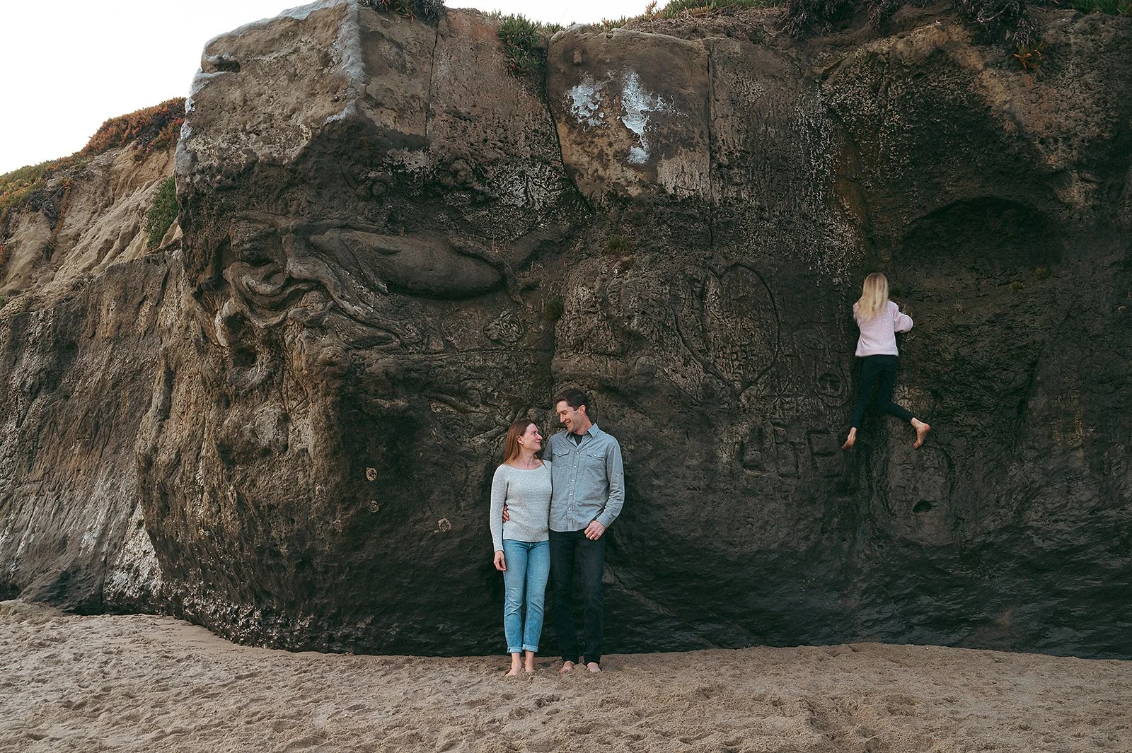 Family smiling while kids climb rocks on the beach in Santa Cruz, California. 
