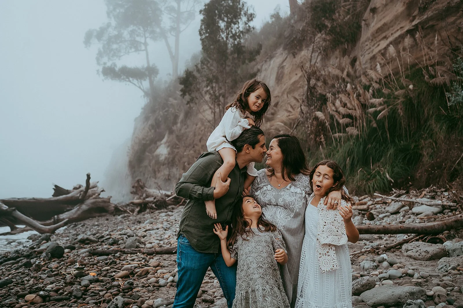 Parents kissing with children on foggy beach in Santa Cruz, California. 