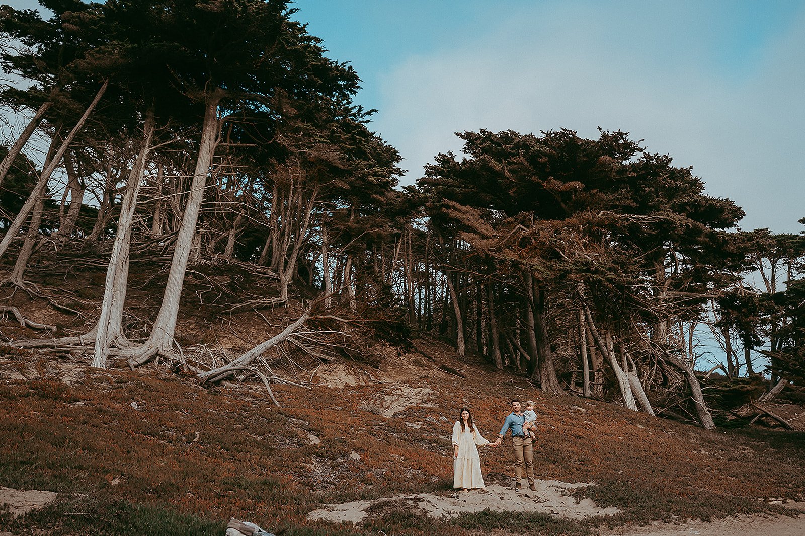 Family smiling and holding hands at Baker Beach in San Francisco, California.