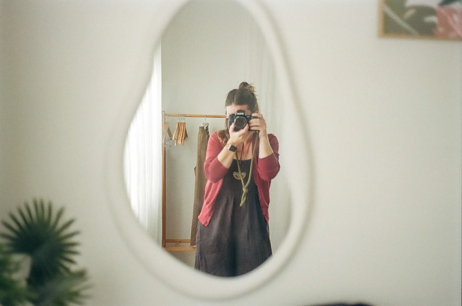 A person taking a photo of herself in an oval mirror on a wall, with minimal bedroom background visible.