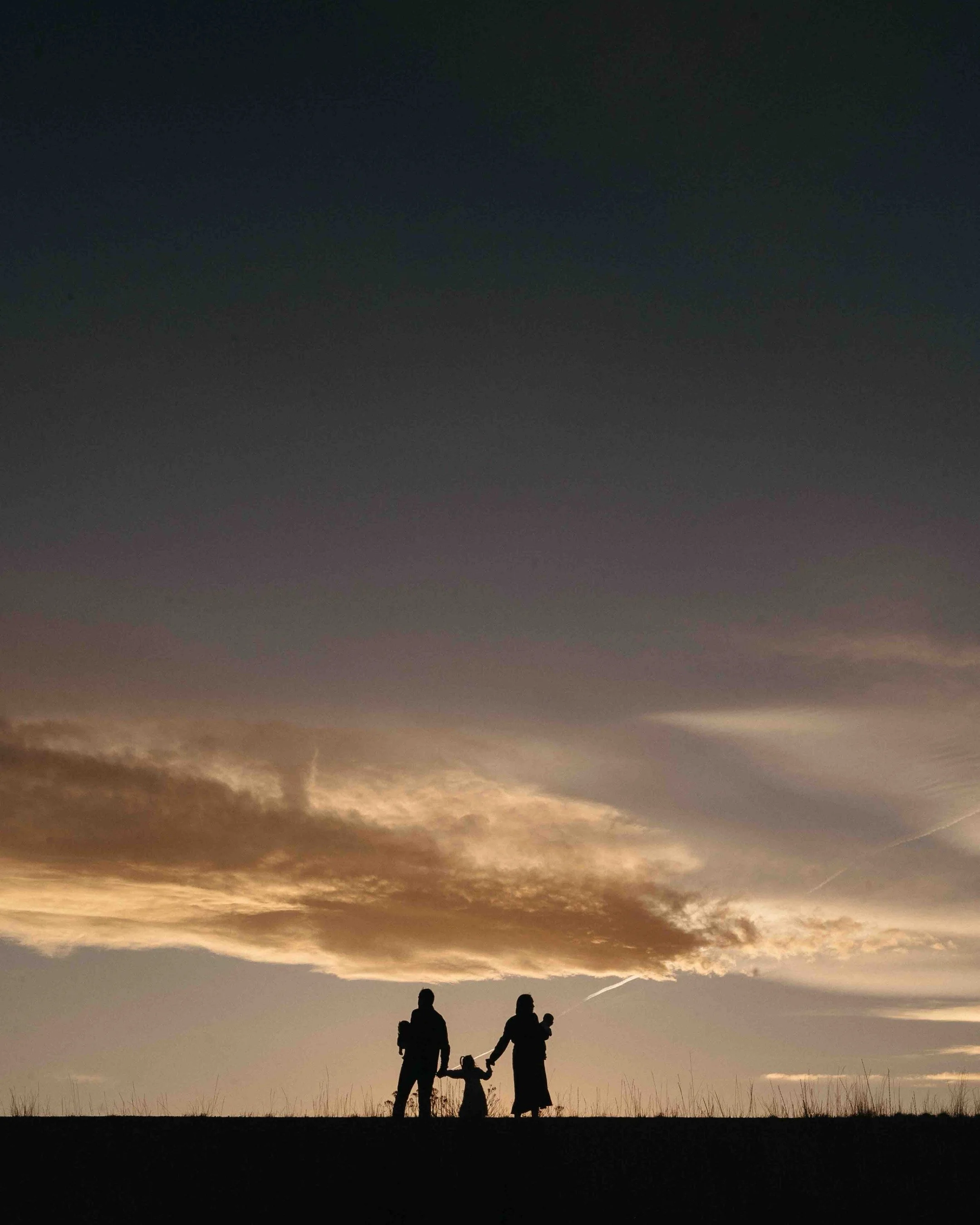 Silhouette of a family with newborn baby twins against sunset in Colorado. 