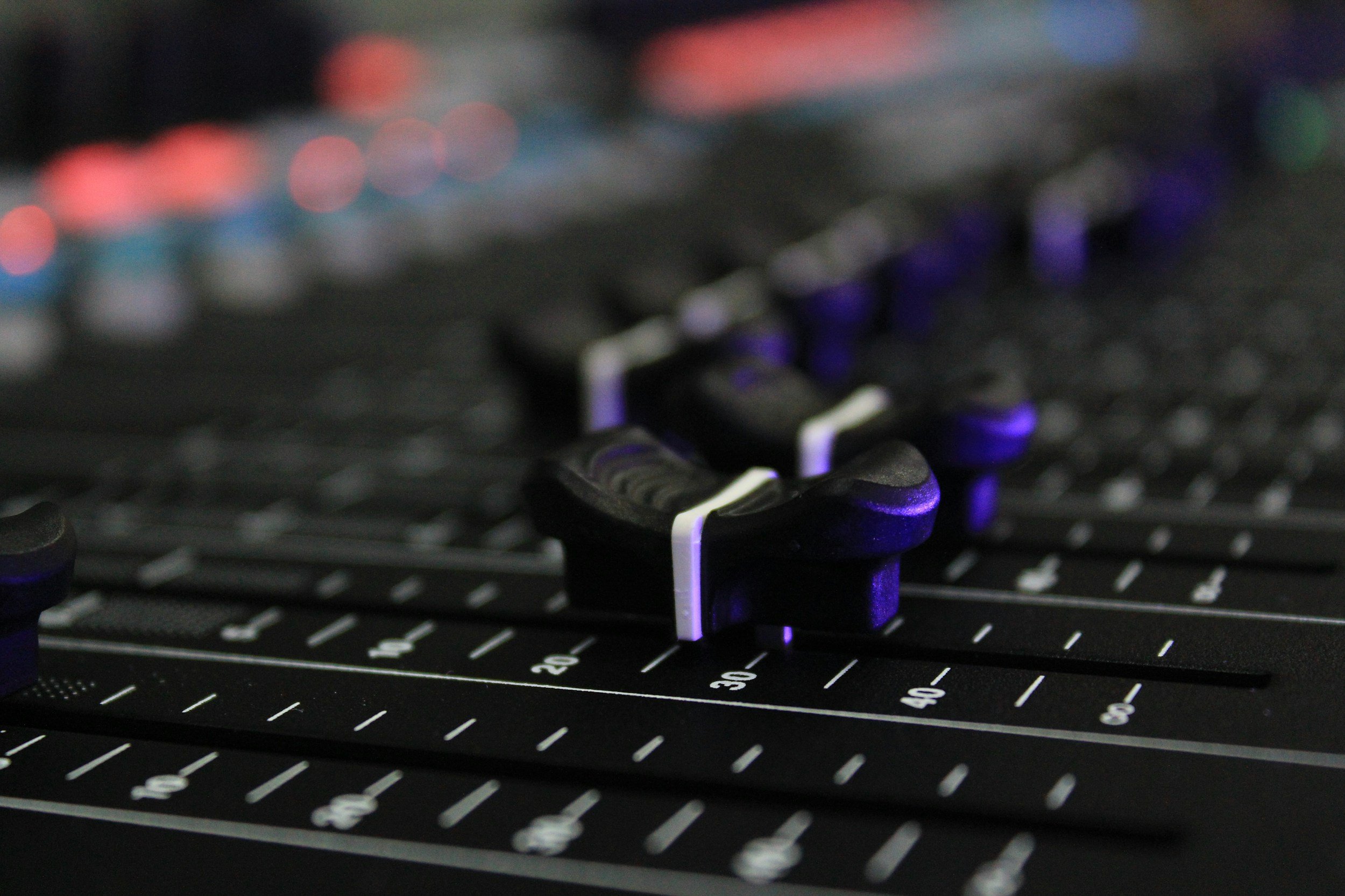 Close-up of illuminated faders on a compact digital mixing console.