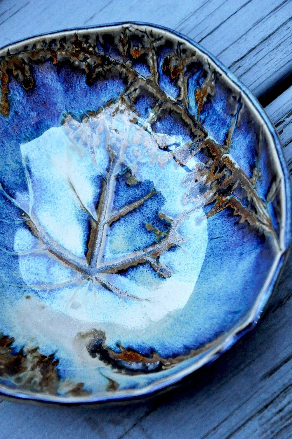 Close-up of a ceramic bowl with a leaf pattern and blue glaze, placed on a wooden surface.
