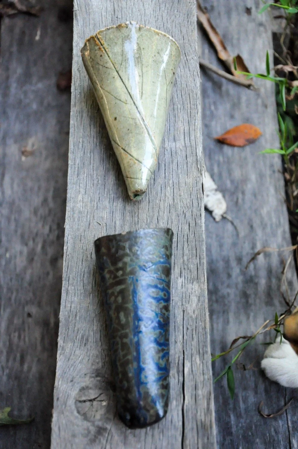 A seashell and a piece of obsidian stone placed on a weathered wooden plank outdoors.