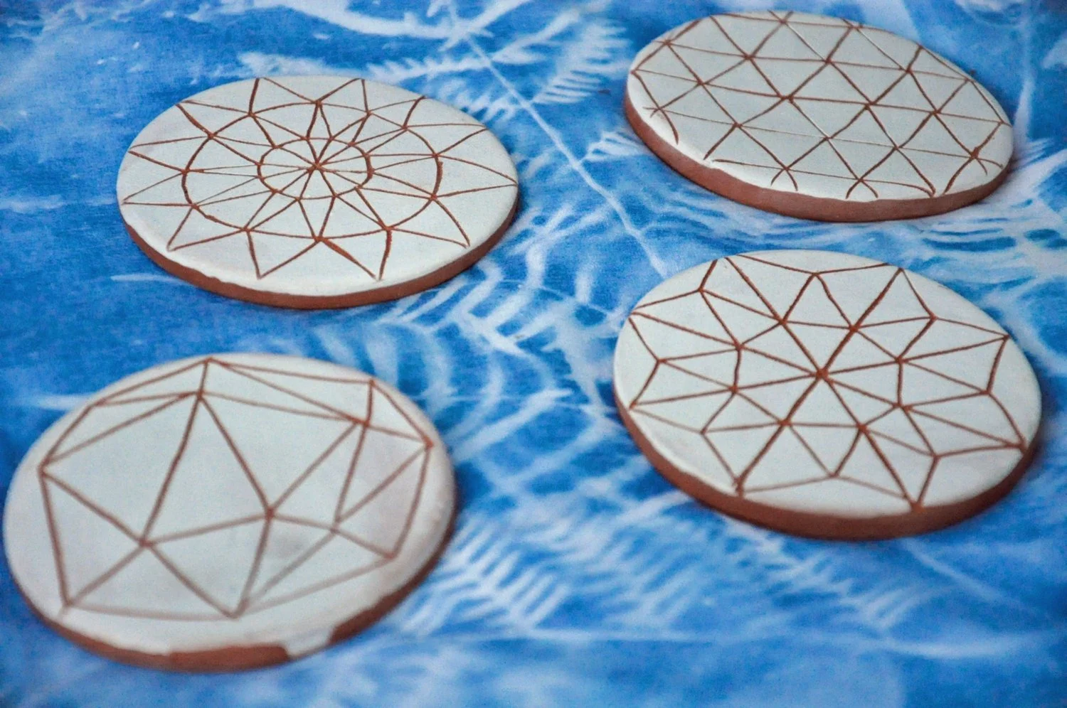 Four round cookies decorated with geometric line patterns on a blue patterned cloth.