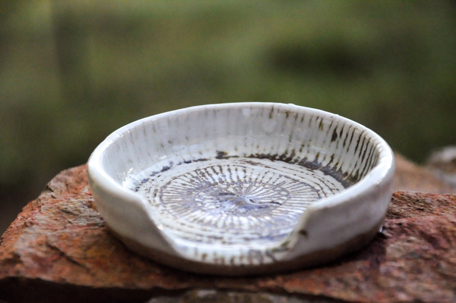 A white ceramic dish with a textured pattern inside, placed on a rough brick surface outdoors with a blurred green background.
