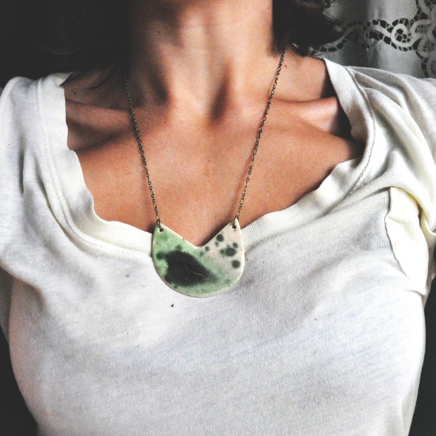 A woman wearing a white shirt with a large, semi-circular green, black, and white patterned necklace.