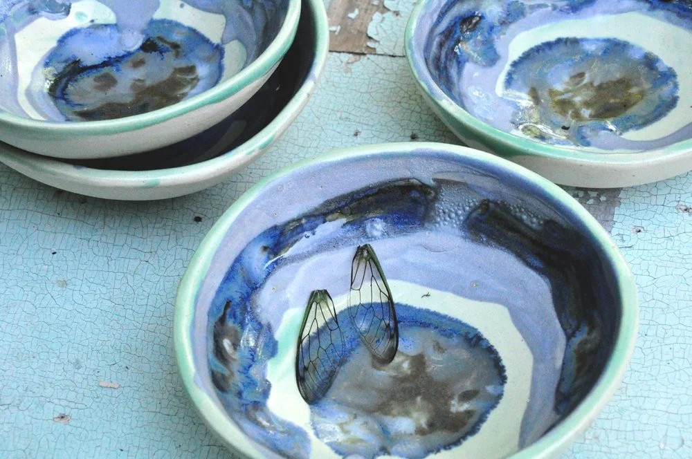 Empty blue and green ceramic bowls with abandoned dragonfly wings inside, placed on a cracked light blue surface.