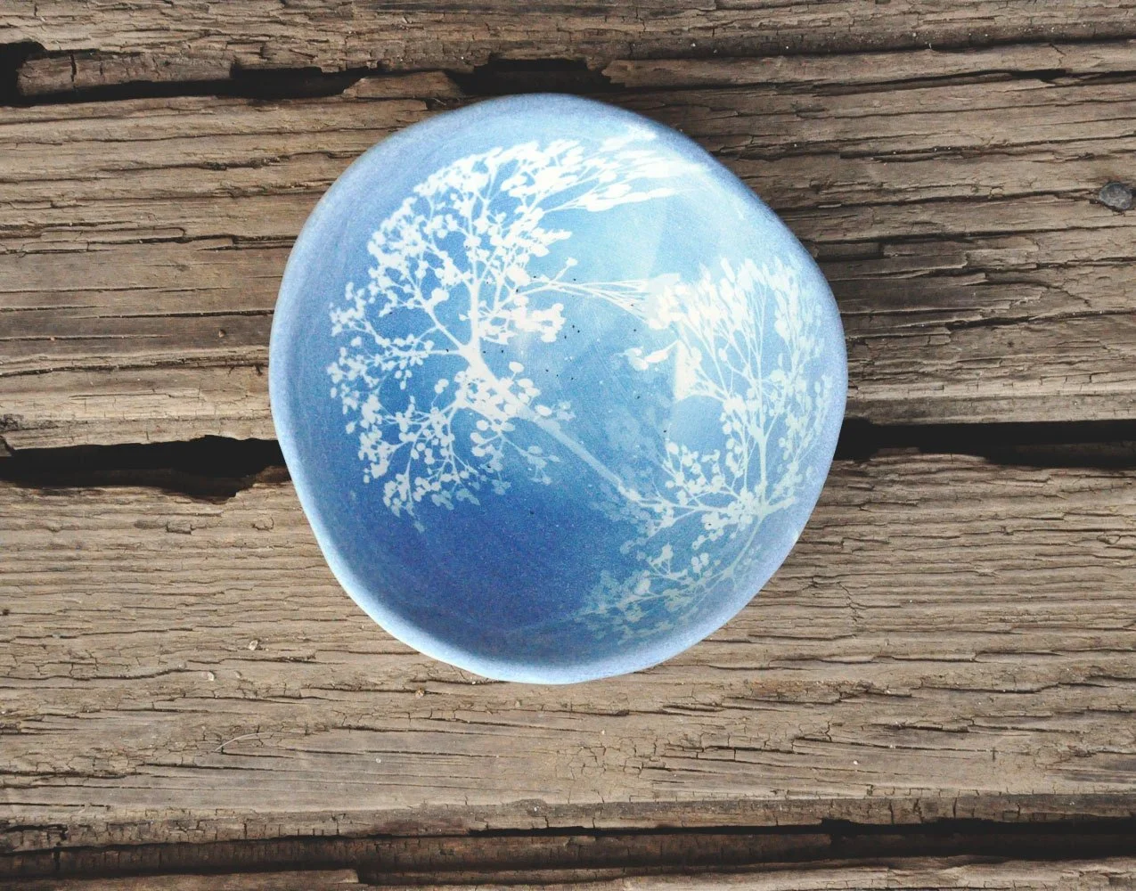 Blue glass paperweight with white botanical design on a weathered wooden surface.