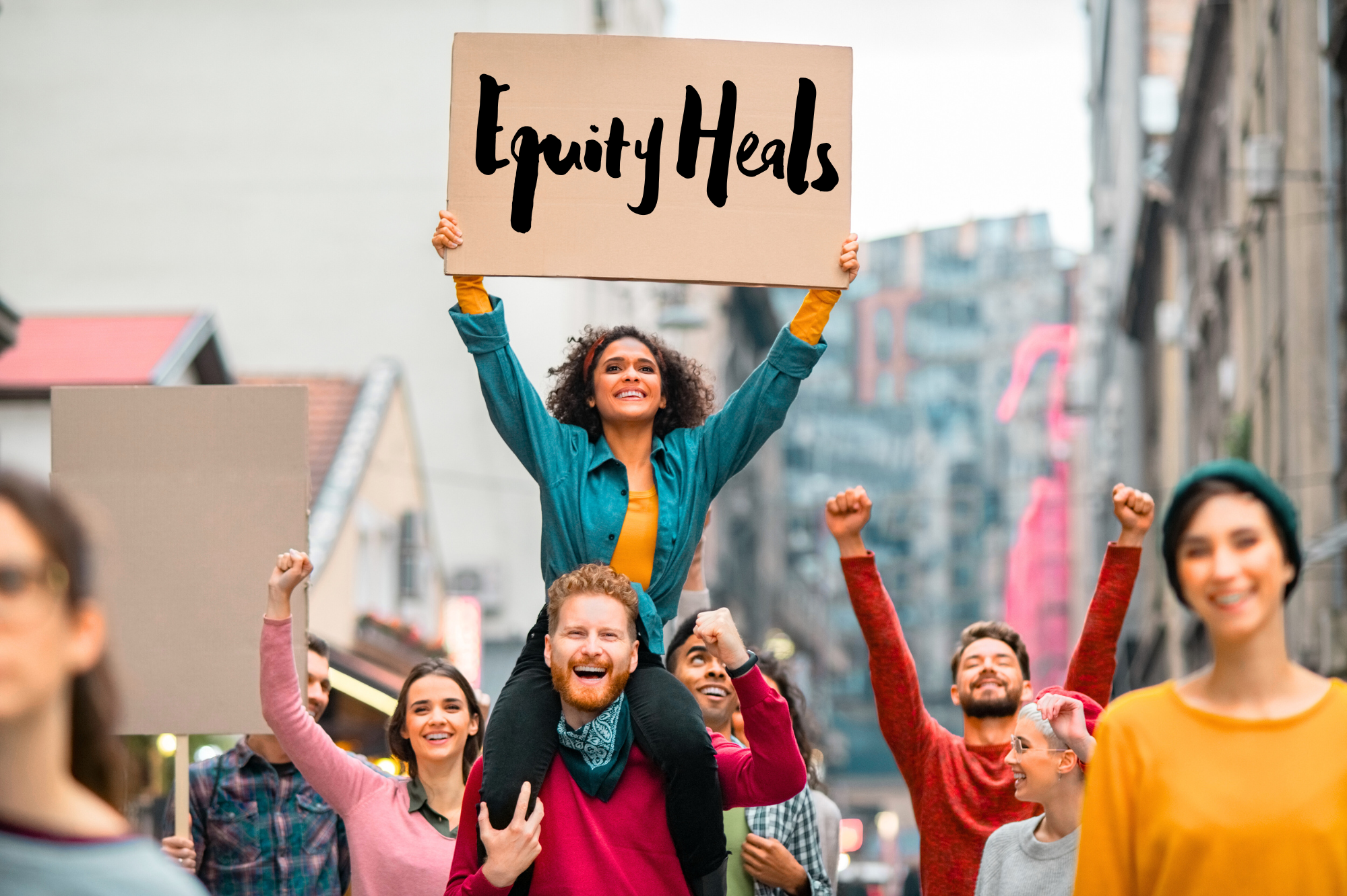 People participating in a protest march, celebrating and holding signs, with a woman on shoulders holding a sign that reads 'Equity Heals' in a city street.