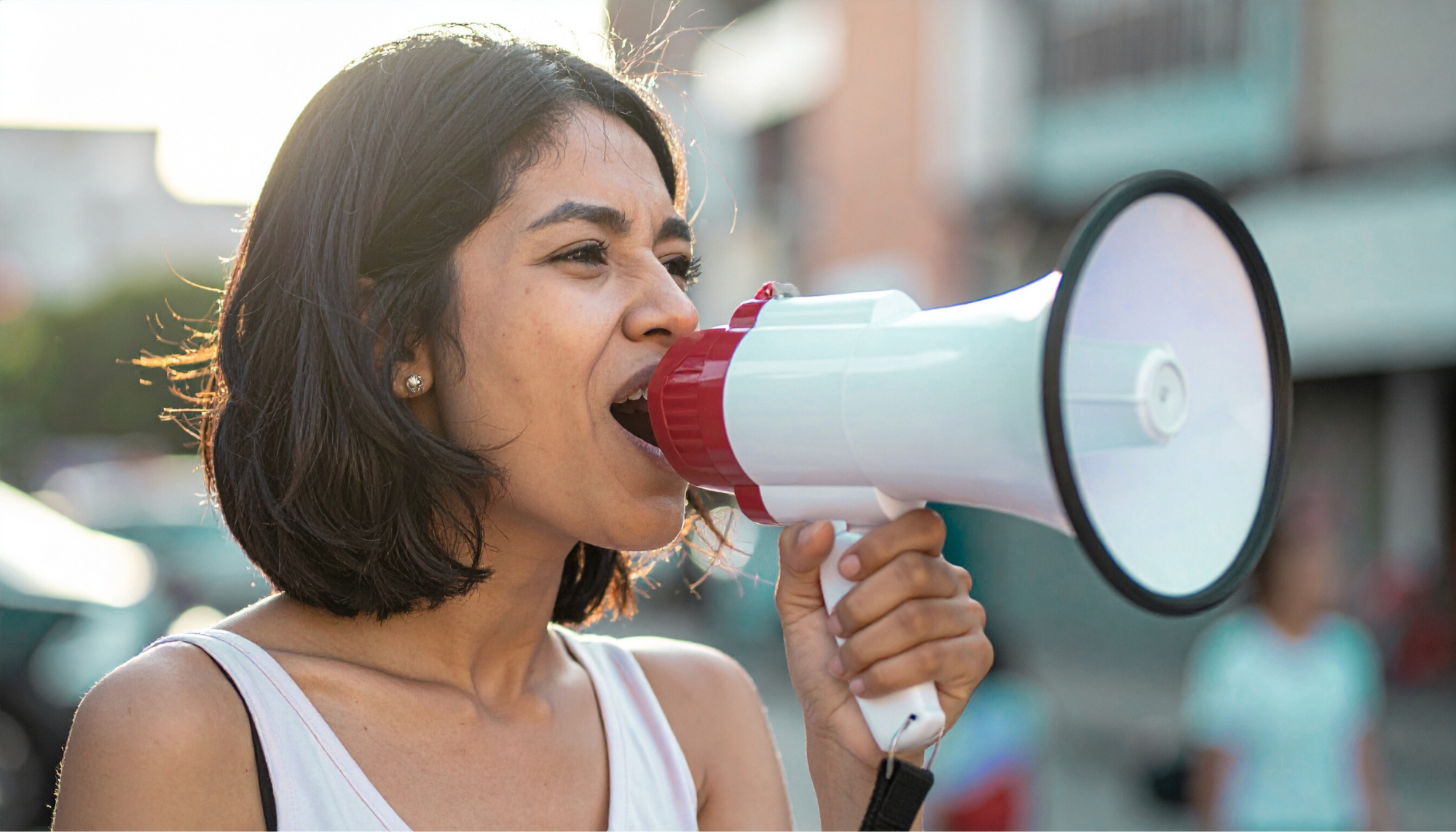 A woman with short dark hair using a megaphone outdoors.