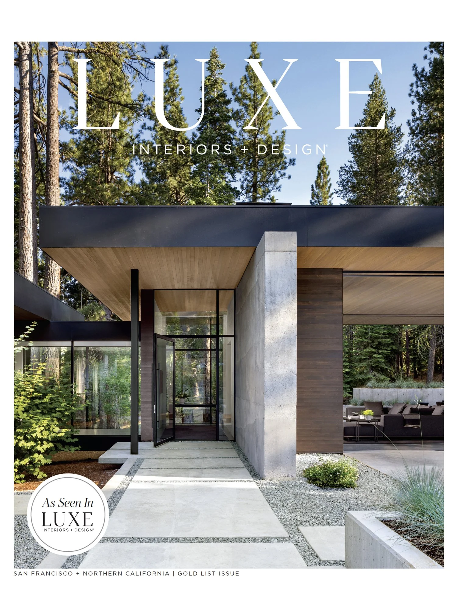 Modern house entrance surrounded by trees with concrete, glass, and wood exterior elements.