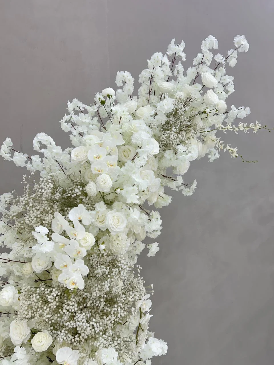 A large arrangement of white flowers including roses, orchids, and baby's breath against a plain gray background.