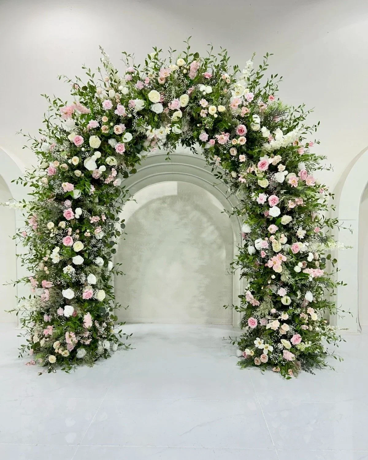 A large floral wreath with pink and white flowers and green foliage against a white wall.