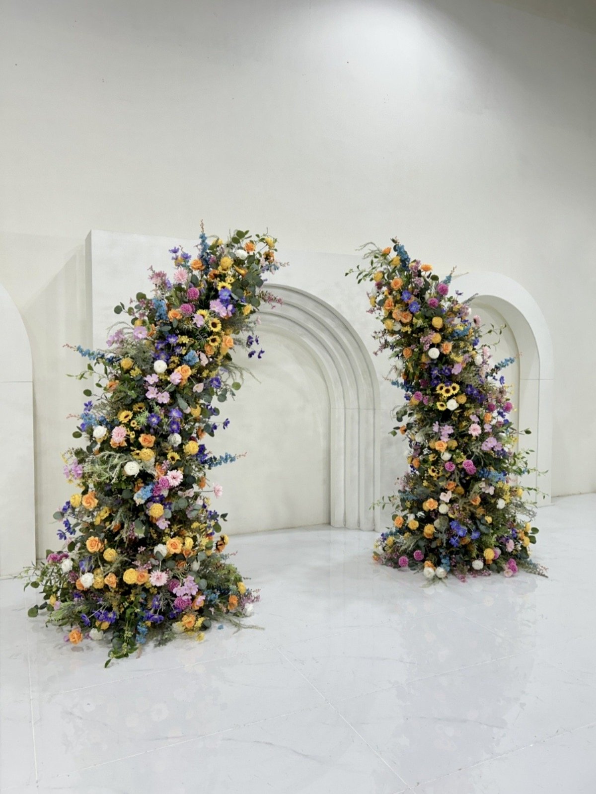 Two large floral arrangements with colorful flowers and greenery on a white background, likely part of a wedding or event decor.