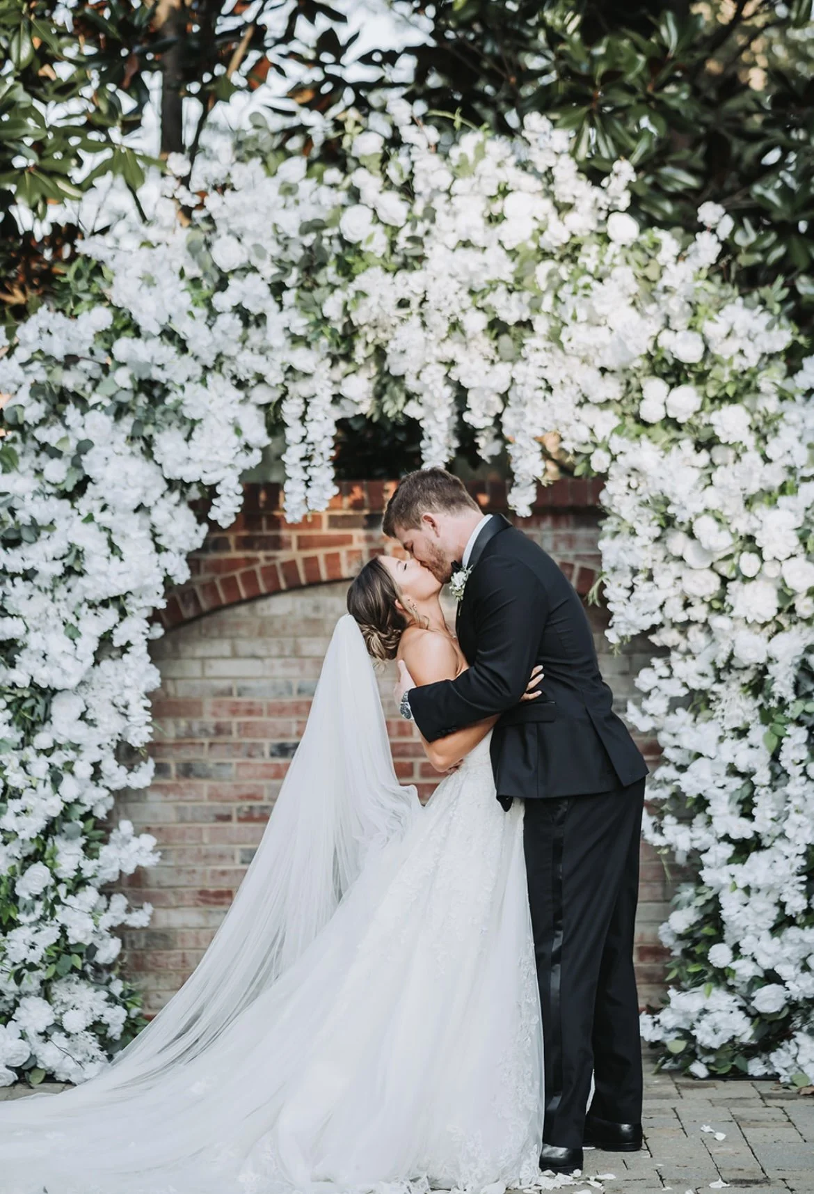 Bride and groom kissing under a floral arch at their wedding.