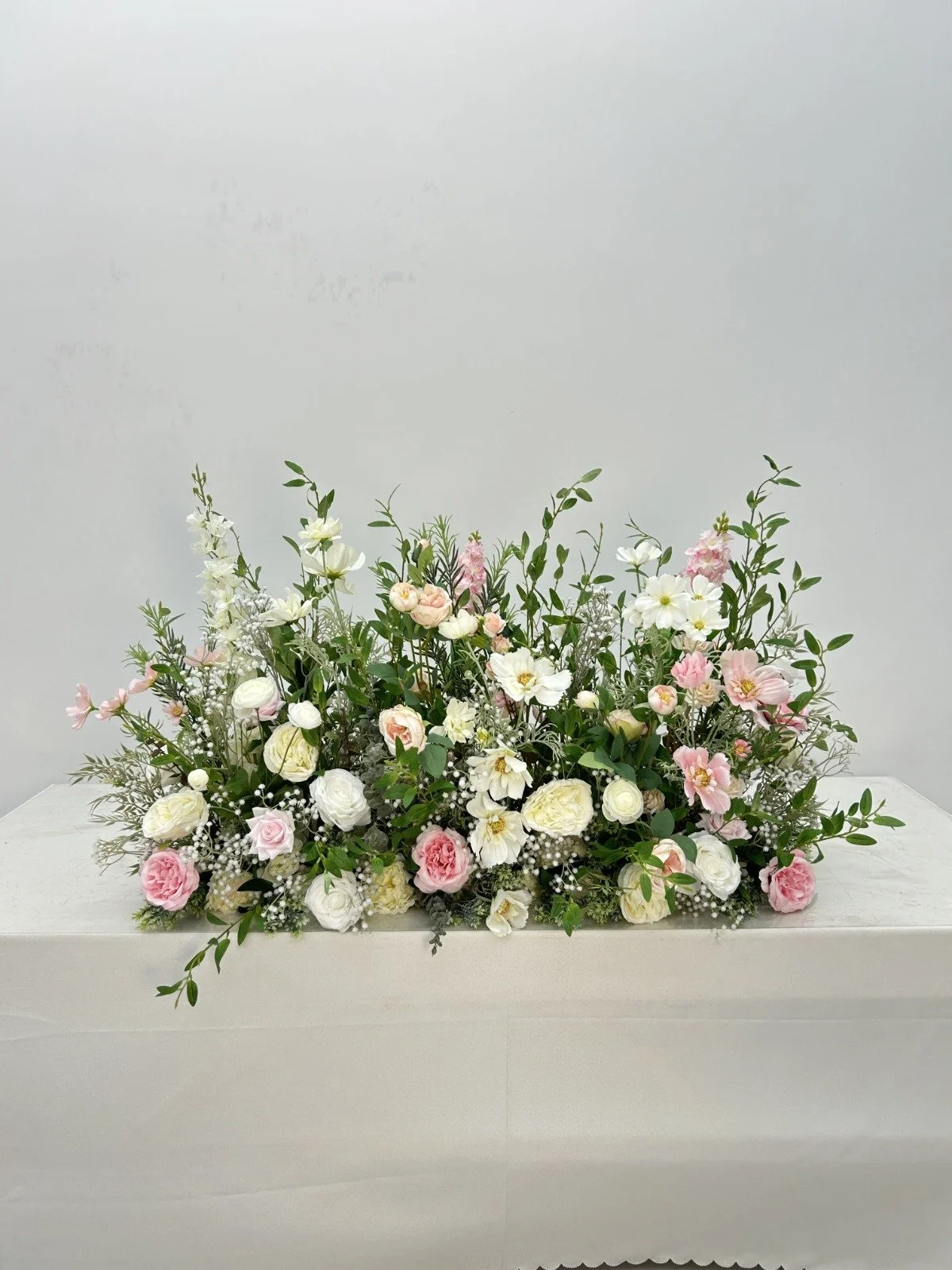 A flower arrangement with pink and white flowers and green foliage on a white surface against a plain white background.