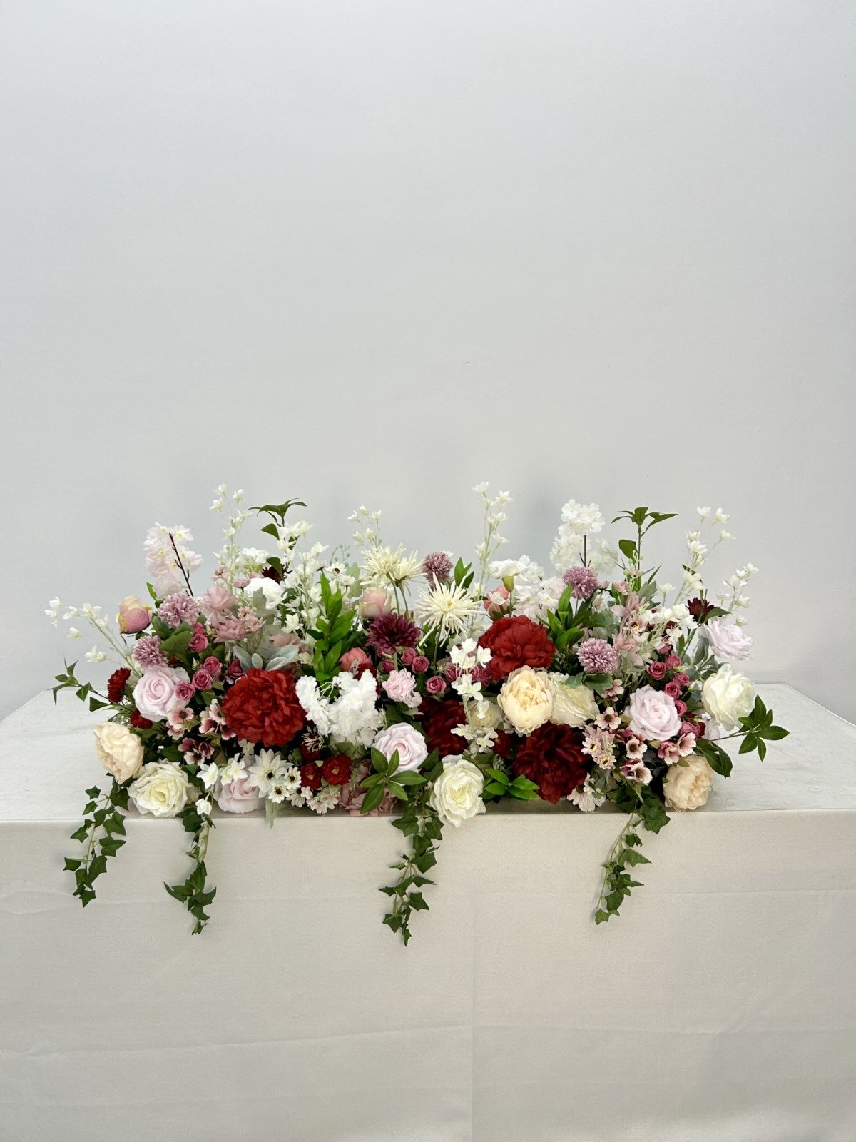 A large arrangement of mixed pink, red, white, and cream-colored flowers with green foliage in a white box.