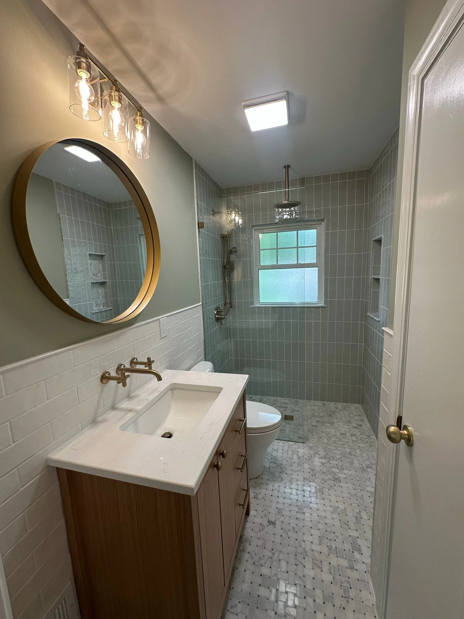 Bathroom with vanities, mirror, toilet, walk-in shower, window, and ceiling lights.