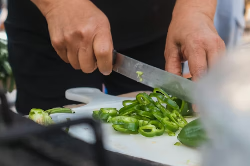 Close up of hands holding knife and chopping green peppers on a white cutting board