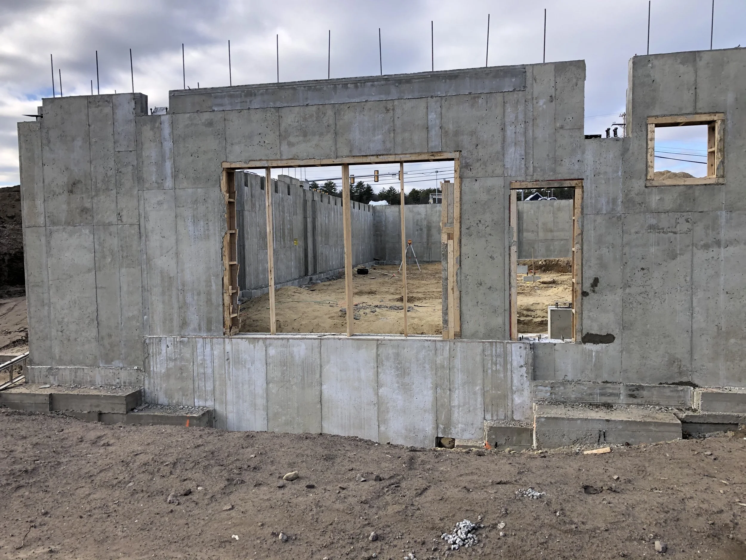 Construction site showing the early stages of building a concrete structure with window and door openings.