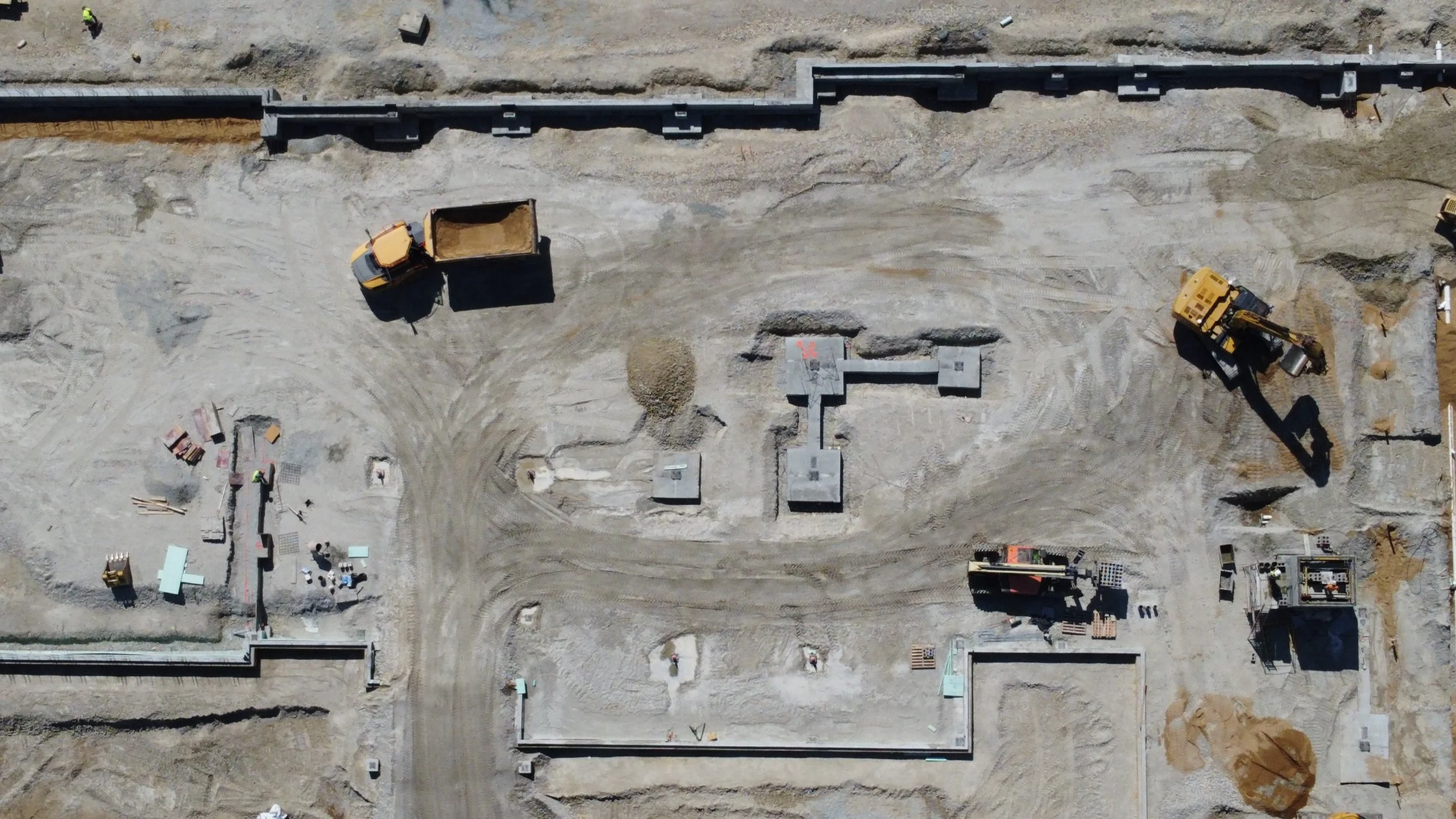 Construction site with construction vehicles, equipment, and partially built structures on a dirt surface.