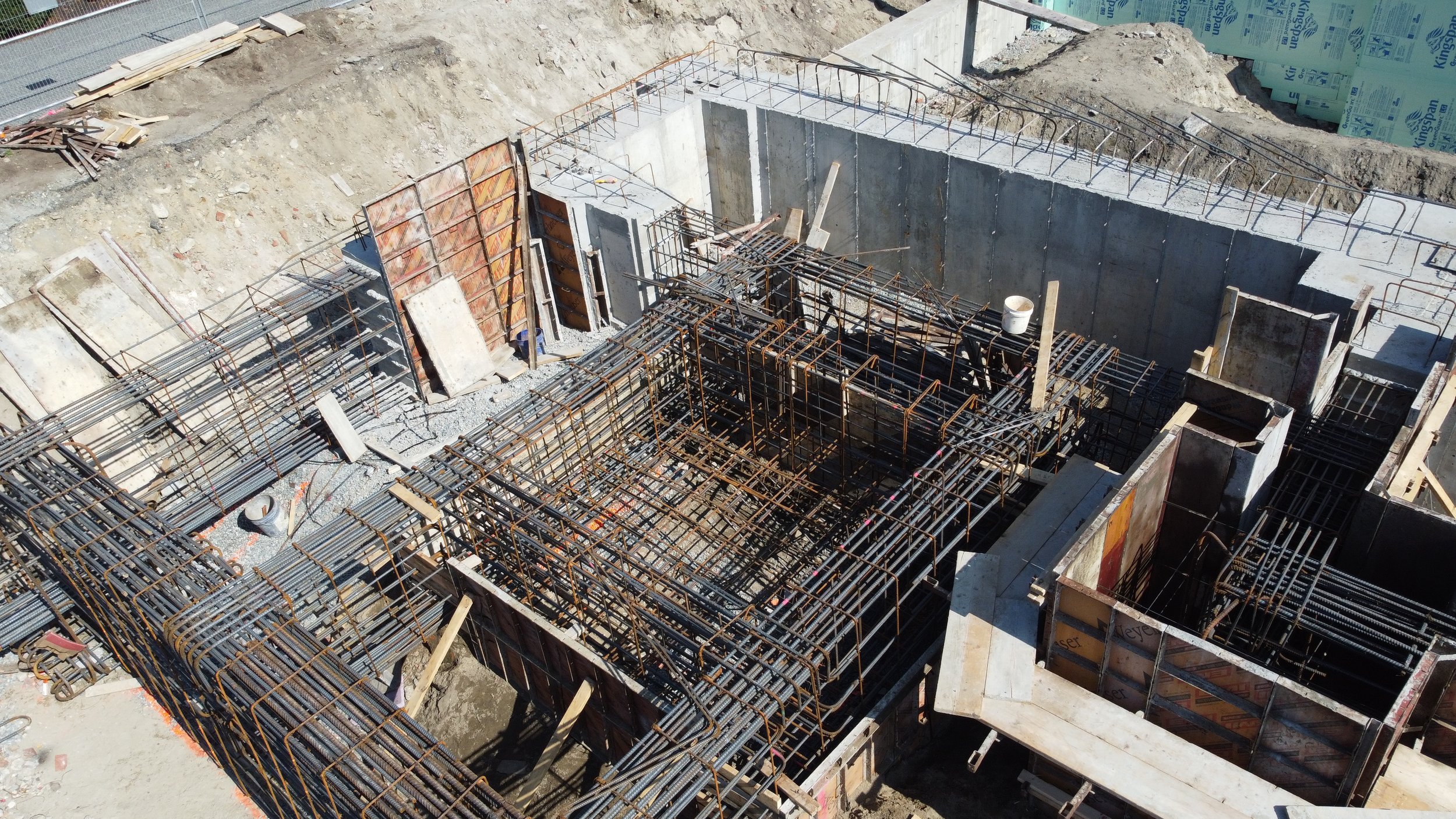 Construction site with steel rebar framework, concrete walls, and building forms at an early stage of building construction.