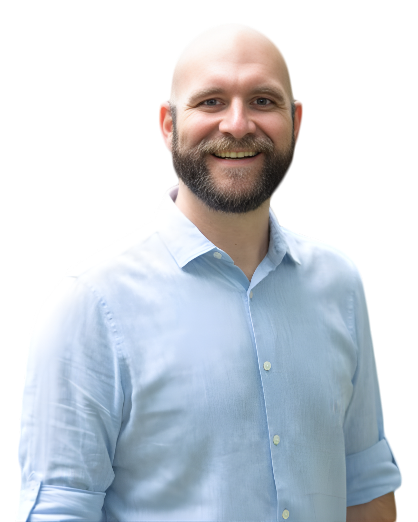 A smiling man with a beard and a shaved head wearing a light blue button-down shirt, standing outdoors.
