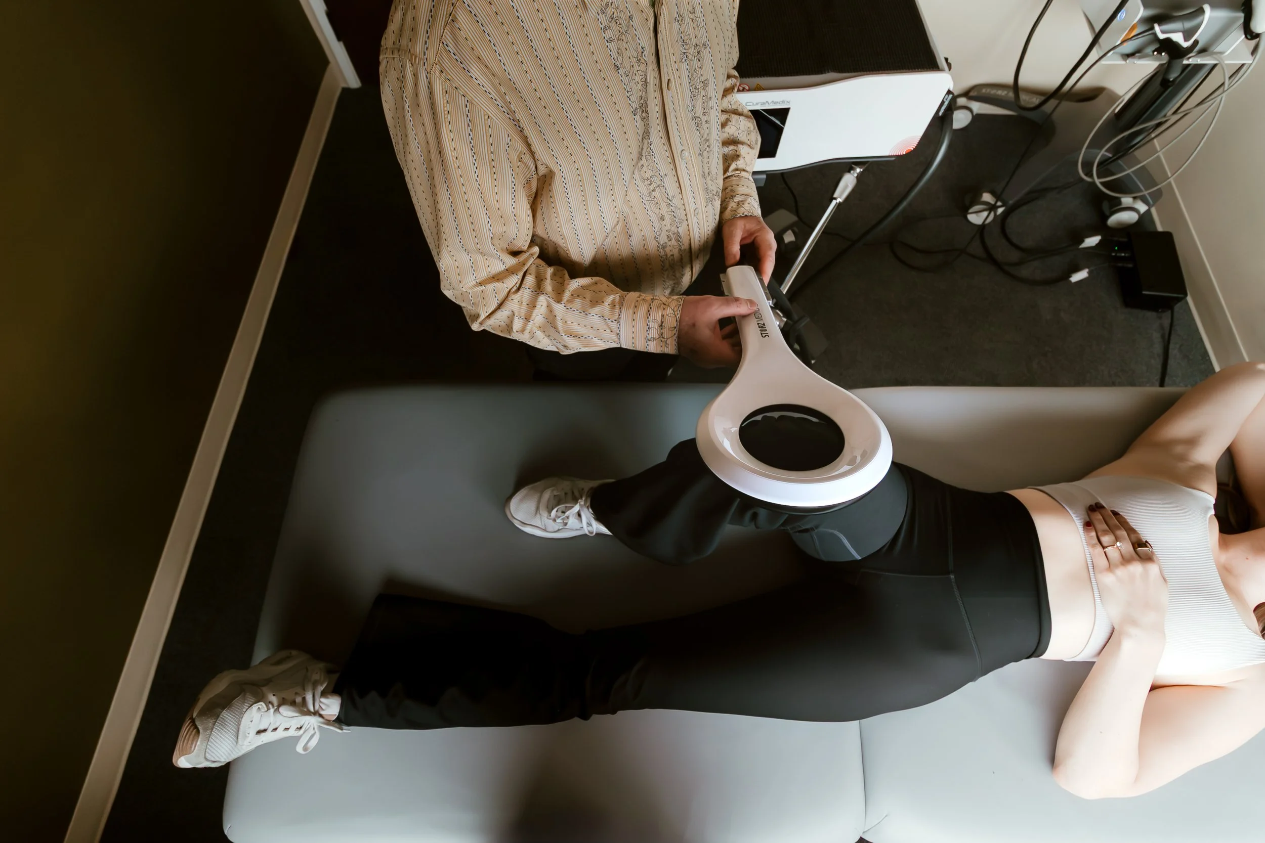 Person undergoing physical therapy or medical examination with a portable ultrasound machine, lying on a treatment table while another person holds the device