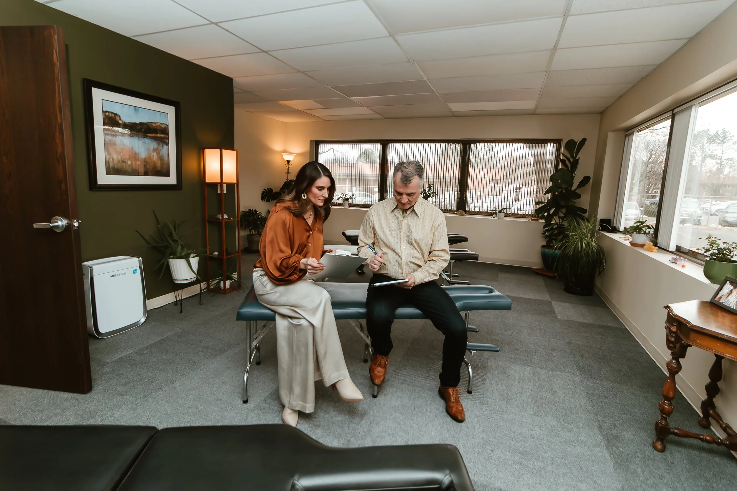 A man and a woman sitting on an examination table in a chiropractor's office, reviewing paperwork together.