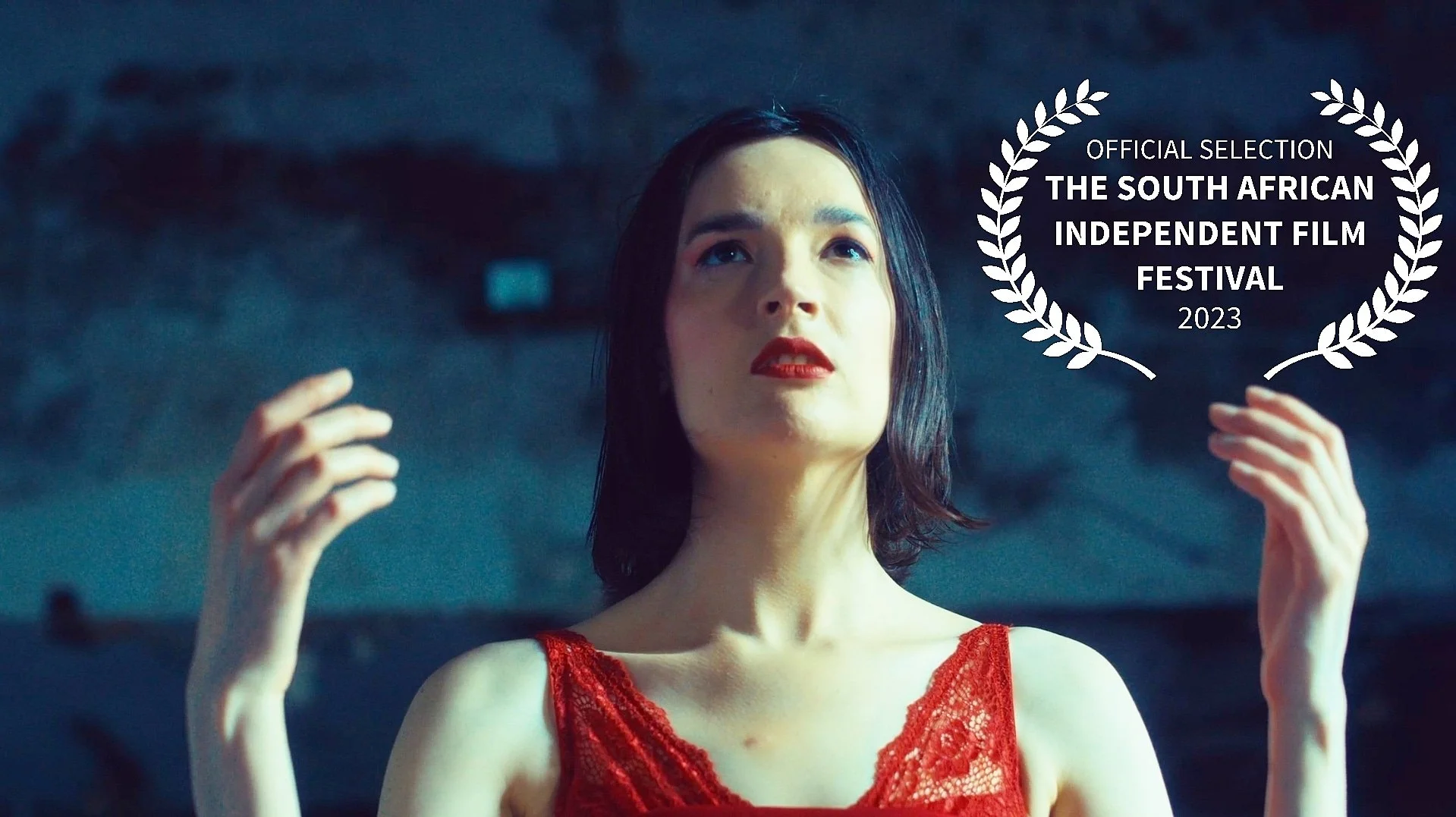 A woman with shoulder-length dark hair wearing a red lace dress, looking upwards with her hands near her face, with a laurel wreath emblem and text indicating her film's selection at the 2023 South African Independent Film Festival.
