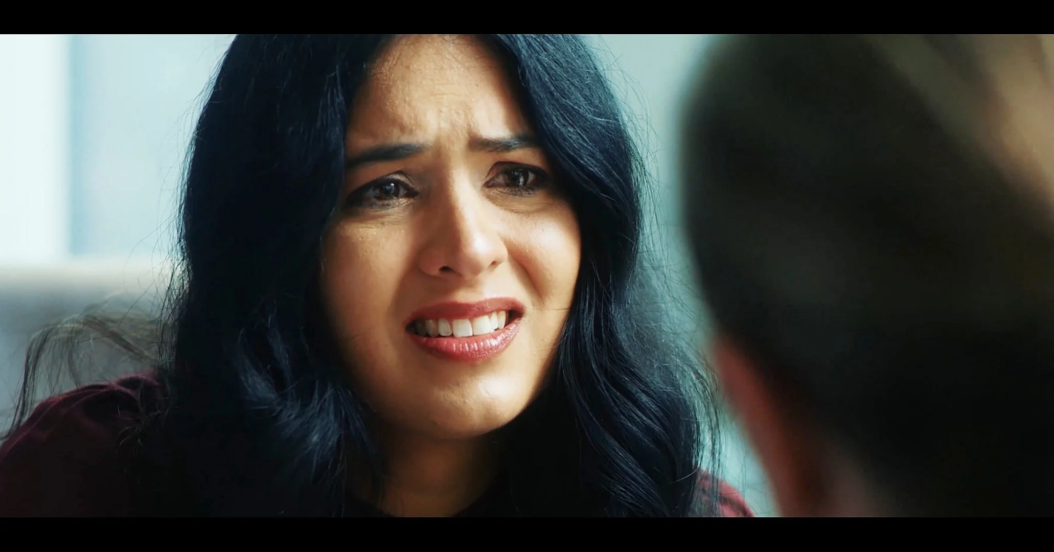 A woman with long black hair and a distressed expression, possibly crying, engaged in a close conversation with a person whose head is partially visible in the foreground.