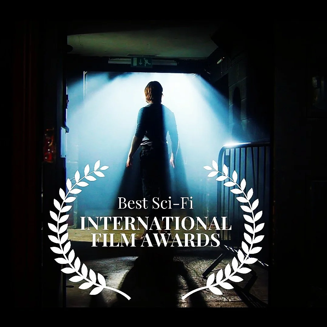 A person standing in a doorway with bright light shining behind them, surrounded by a laurel wreath and text that reads "Best Sci-Fi International Film Awards."