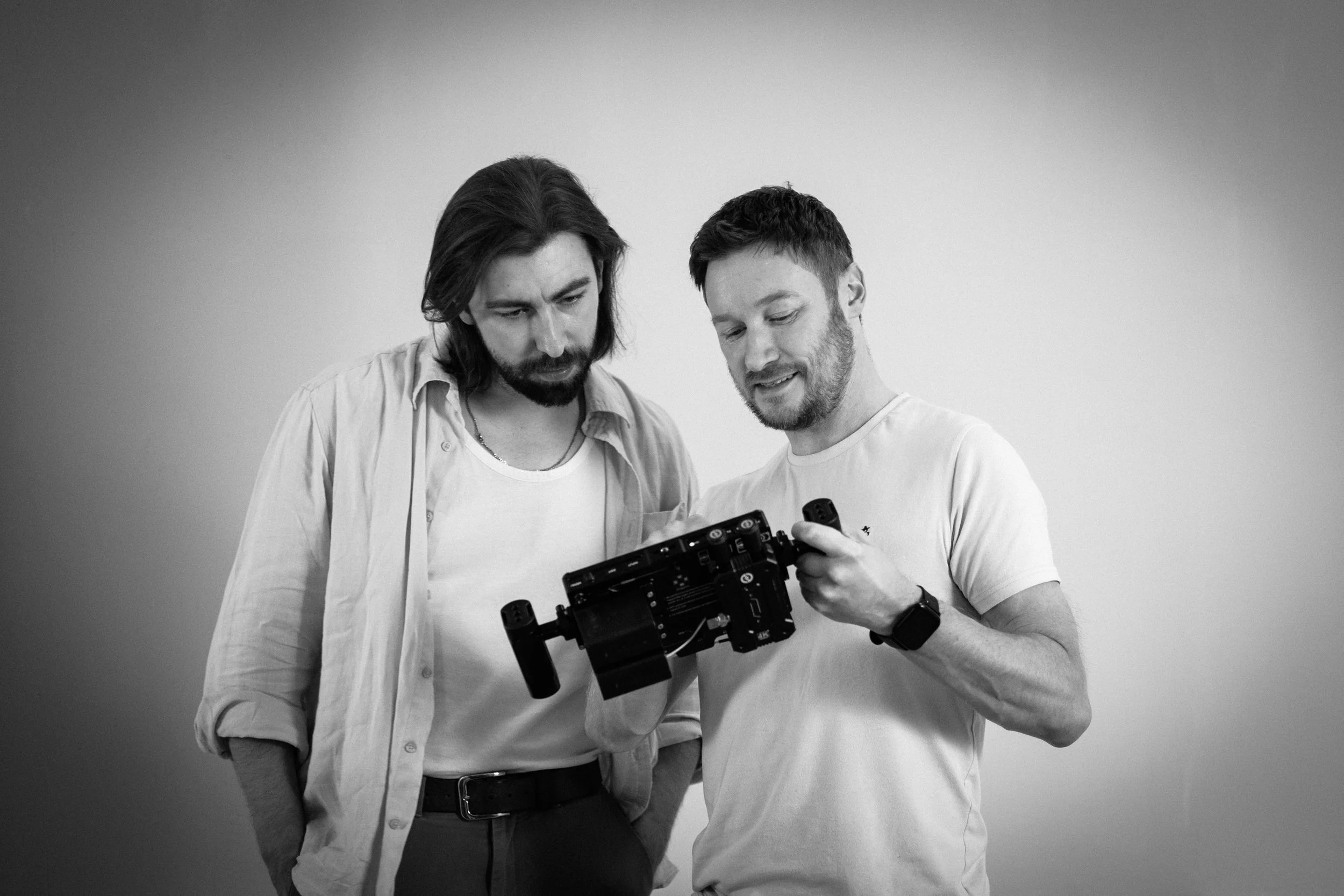 Two men look at a camera rig together against a plain wall.