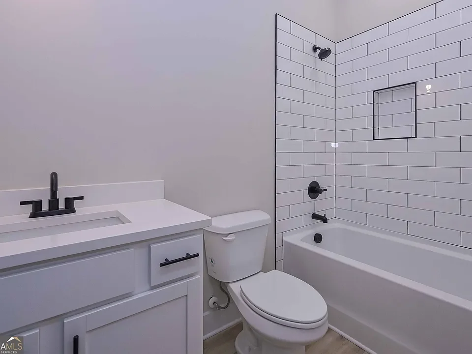 Modern bathroom with white vanity, black fixtures, toilet, and bathtub with white subway tile surround.