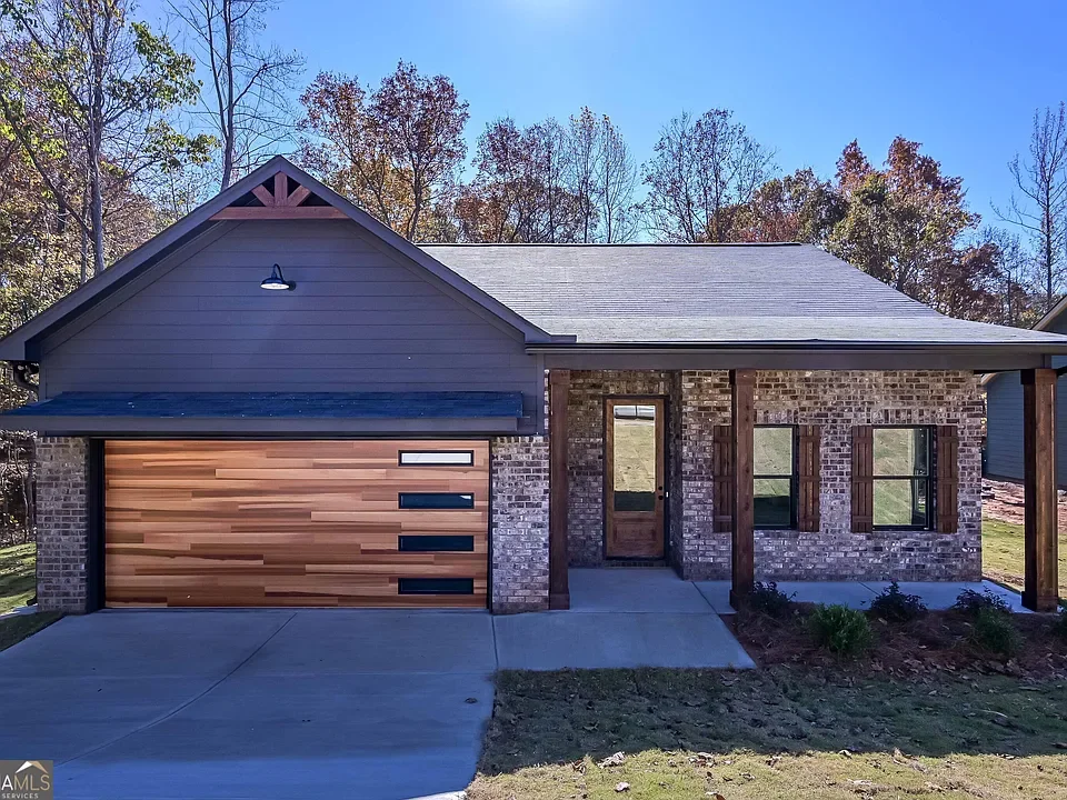Photo of a modern house with a brick exterior, wooden accents, and a front porch with pillars, set against a backdrop of trees and a clear blue sky.