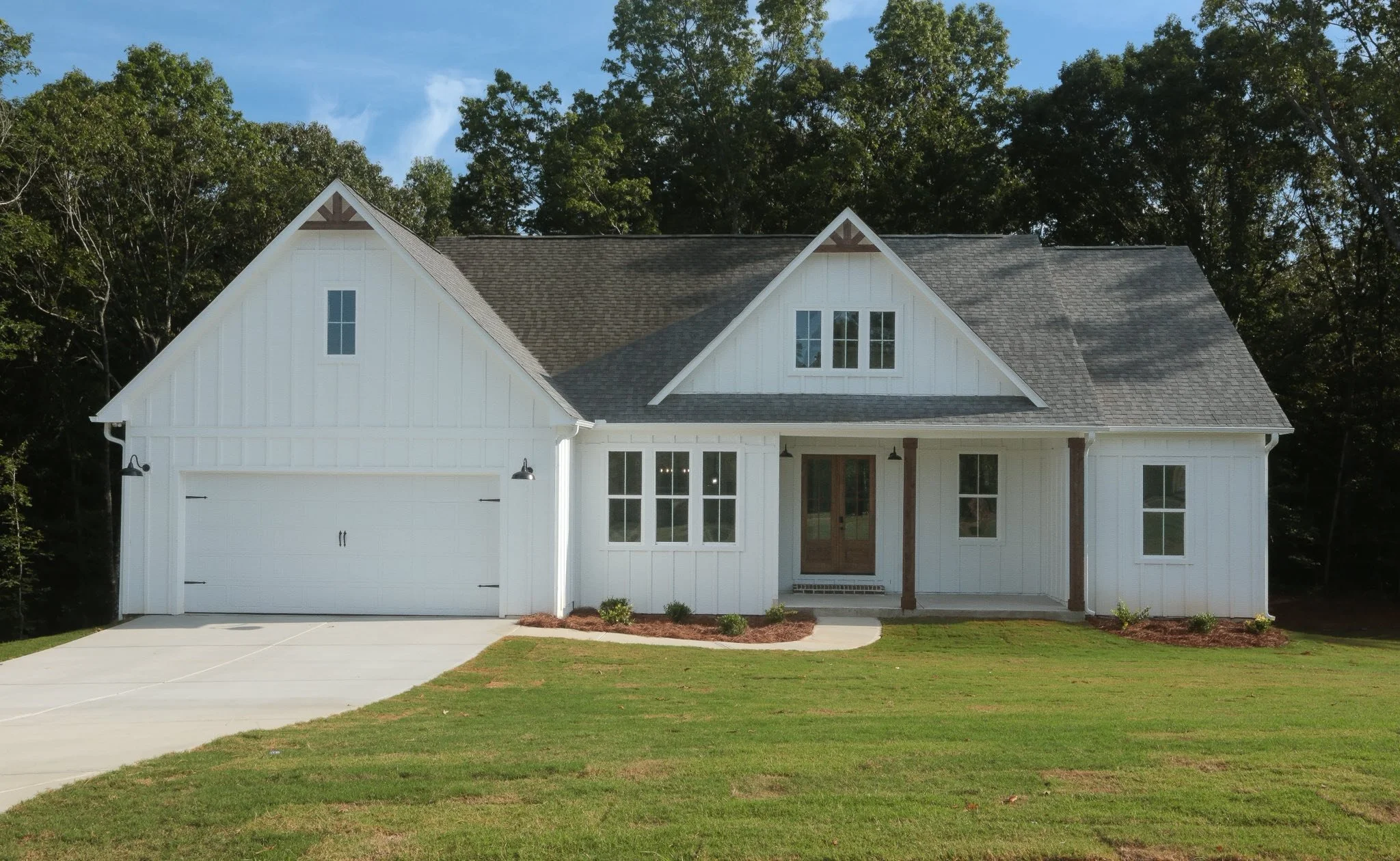 White farmhouse-style house with a gable roof, front porch, and attached garage, surrounded by a well-maintained lawn and trees in the background.