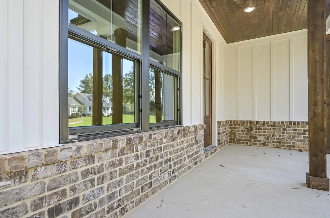 Covered porch with large window, brick ledge, and wooden ceiling, under construction.