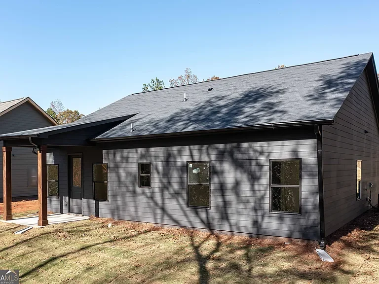 New gray house with a sloped roof and multiple windows, shadow of a tree on the exterior wall, with a small porch area supported by wooden posts.