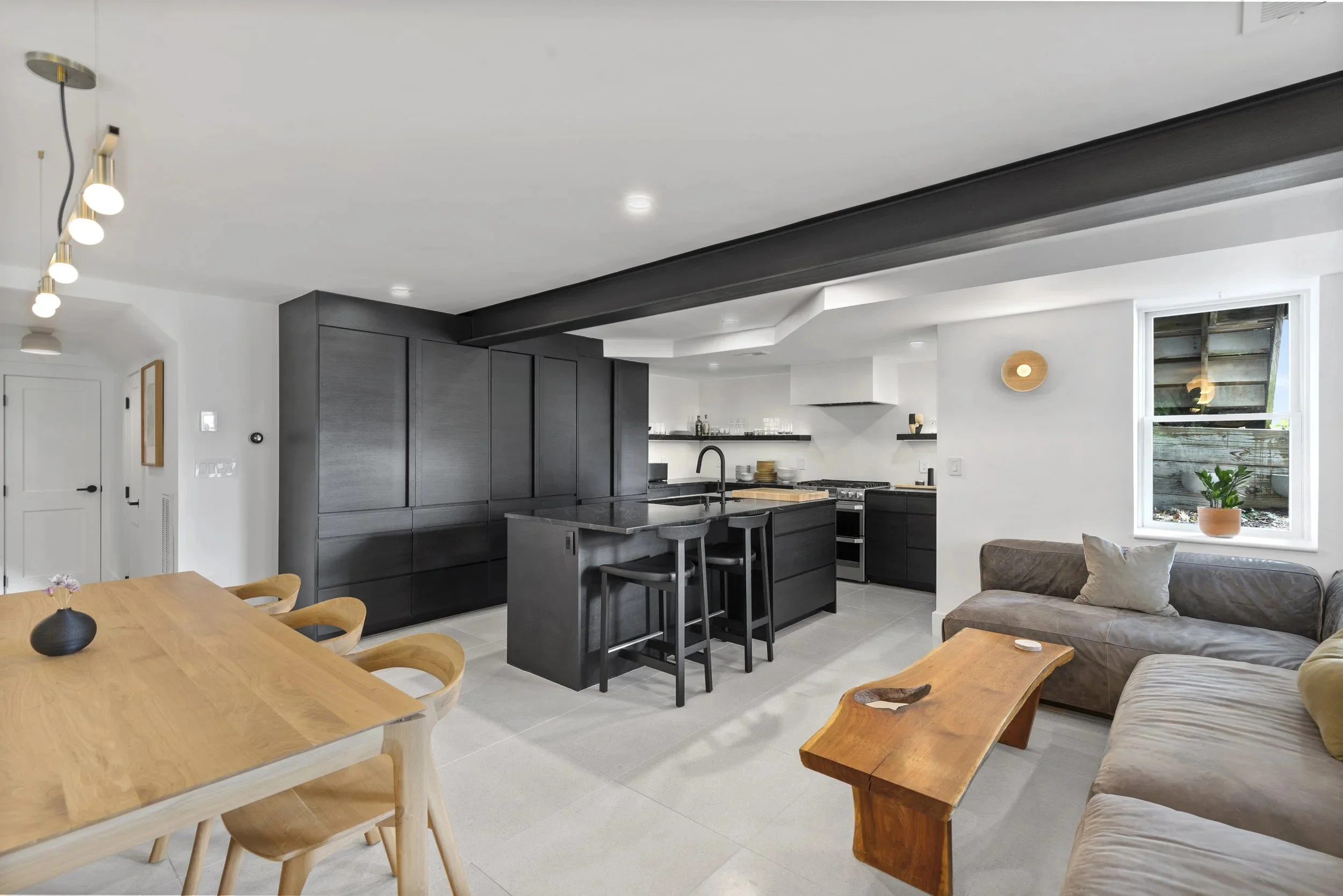 Modern open-plan kitchen and living room with black cabinetry, a wooden dining table, a beige sofa, and minimalist decor.