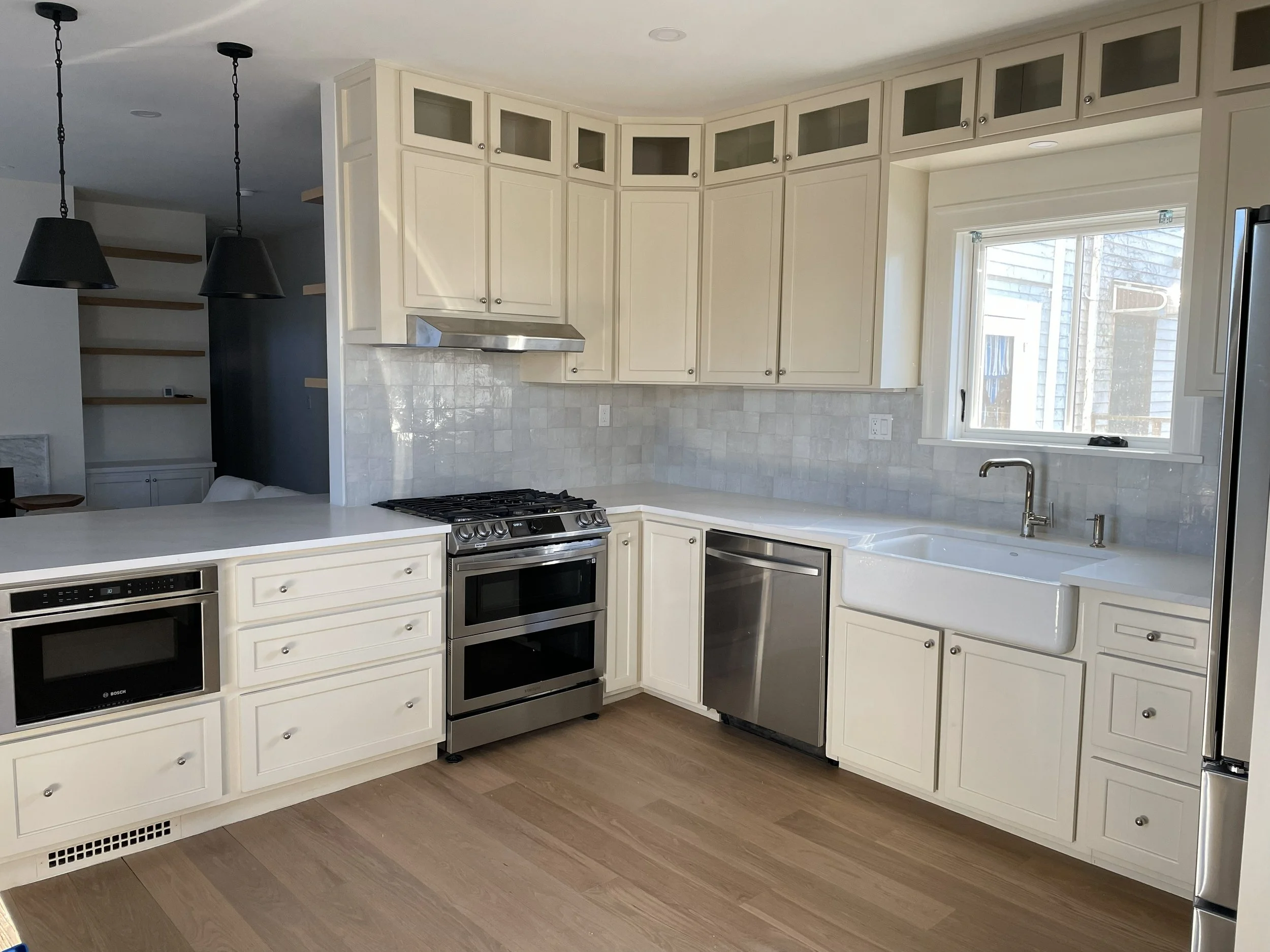 Kitchen with white cabinets, stainless steel appliances, a large farmhouse sink, light wood flooring, and a window above the sink.