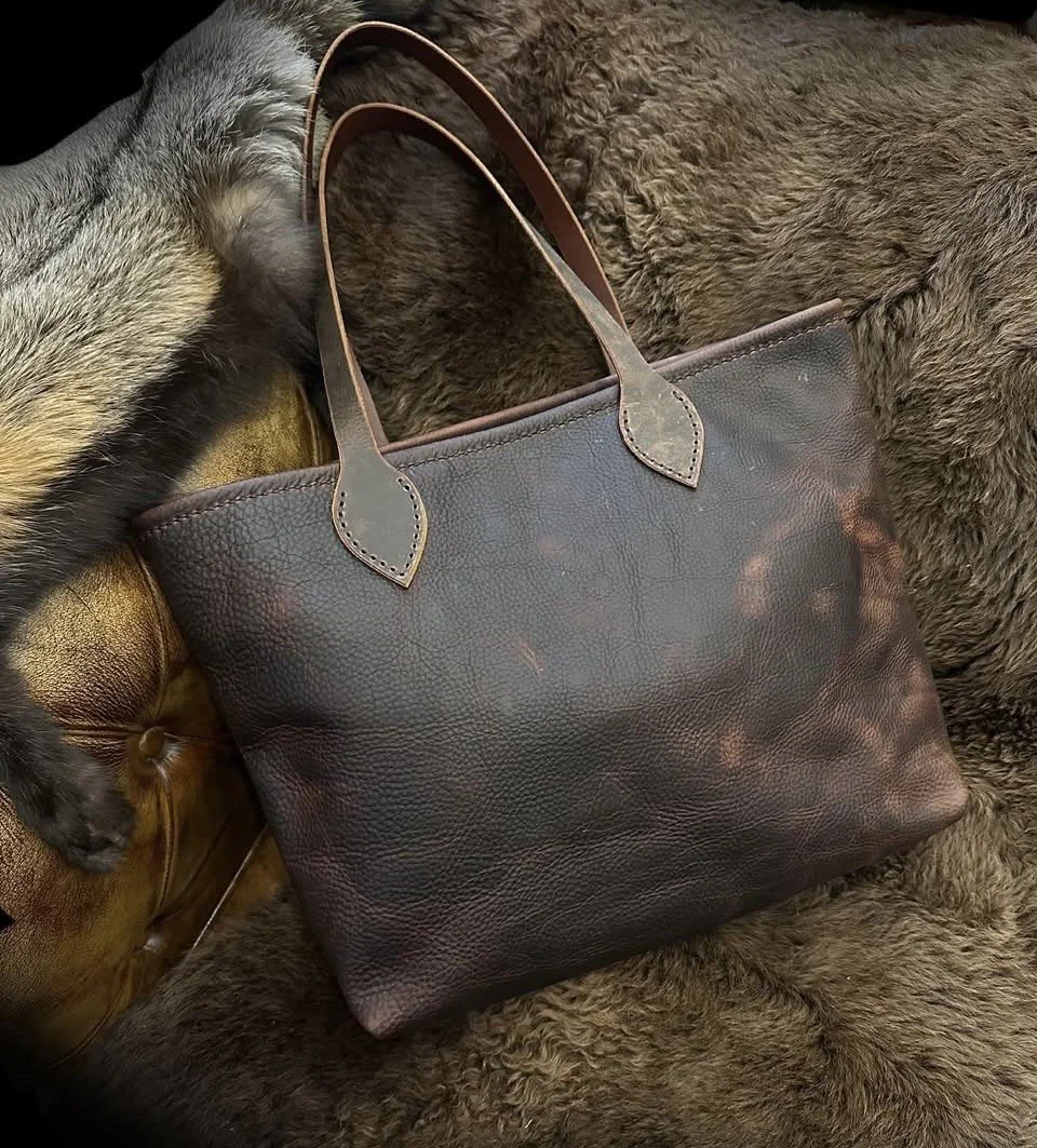 Dark brown leather tote bag with long handles resting on a brown fur coat.