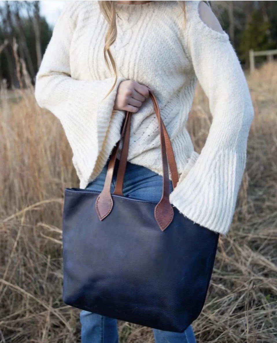 Woman wearing a white knit sweater and jeans, carrying a large navy leather tote bag outdoors