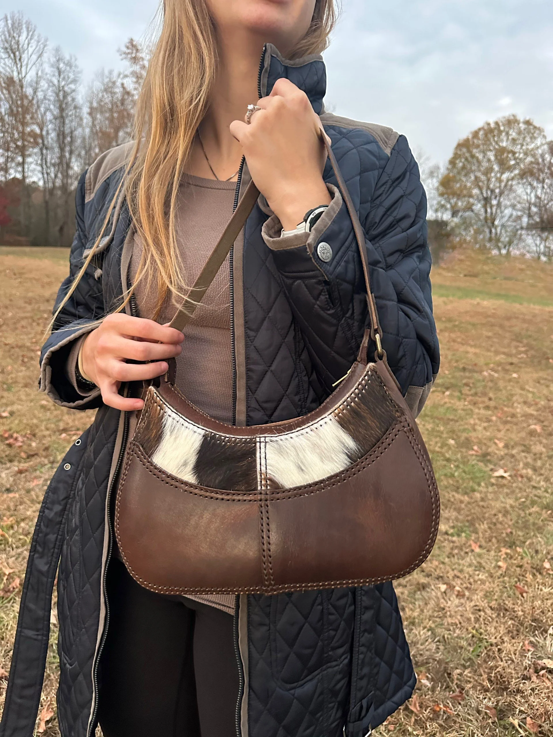 Close-up of a woman wearing a navy quilted jacket and carrying a large brown leather tote bag outdoors