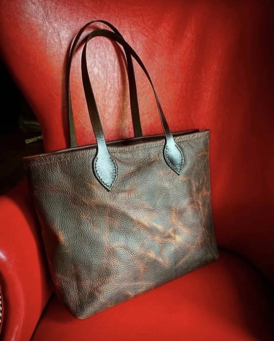 Brown leather tote bag with long handles displayed against a red leather background