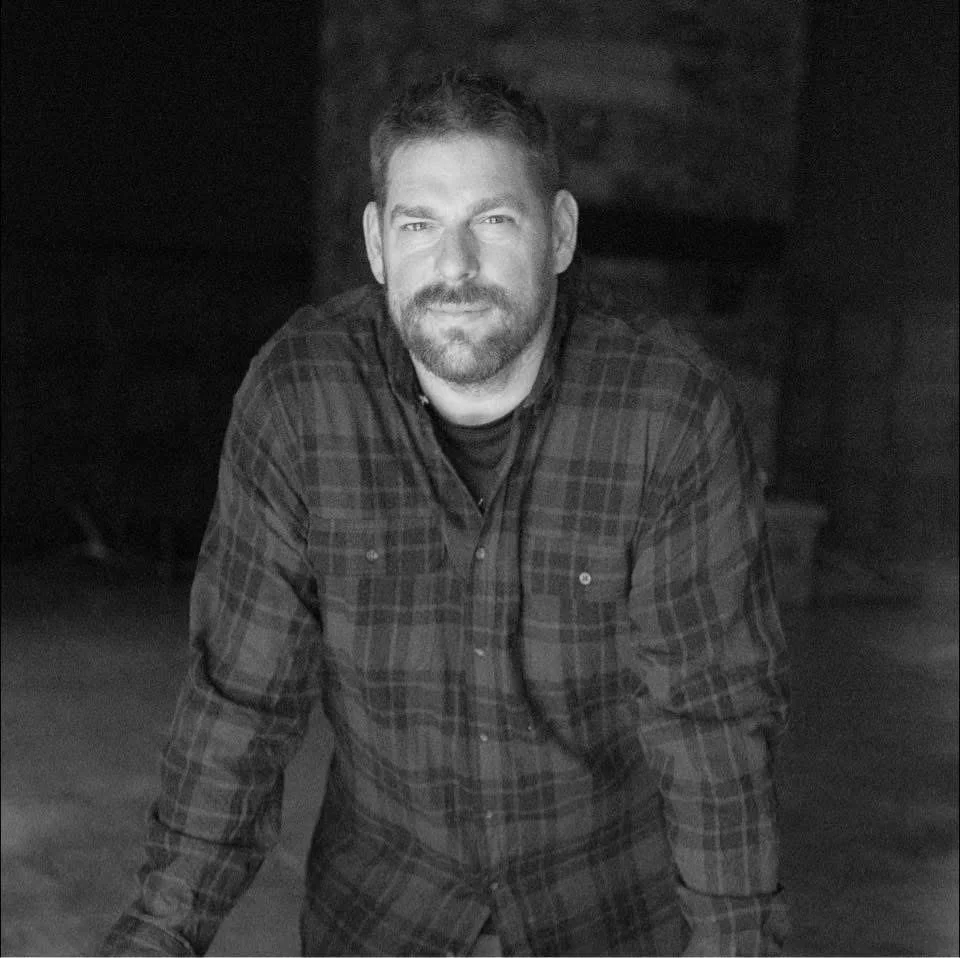 Black-and-white portrait of a bearded man wearing a plaid flannel shirt outdoors