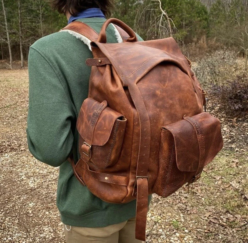 Person wearing a large vintage brown leather backpack with multiple pockets outdoors